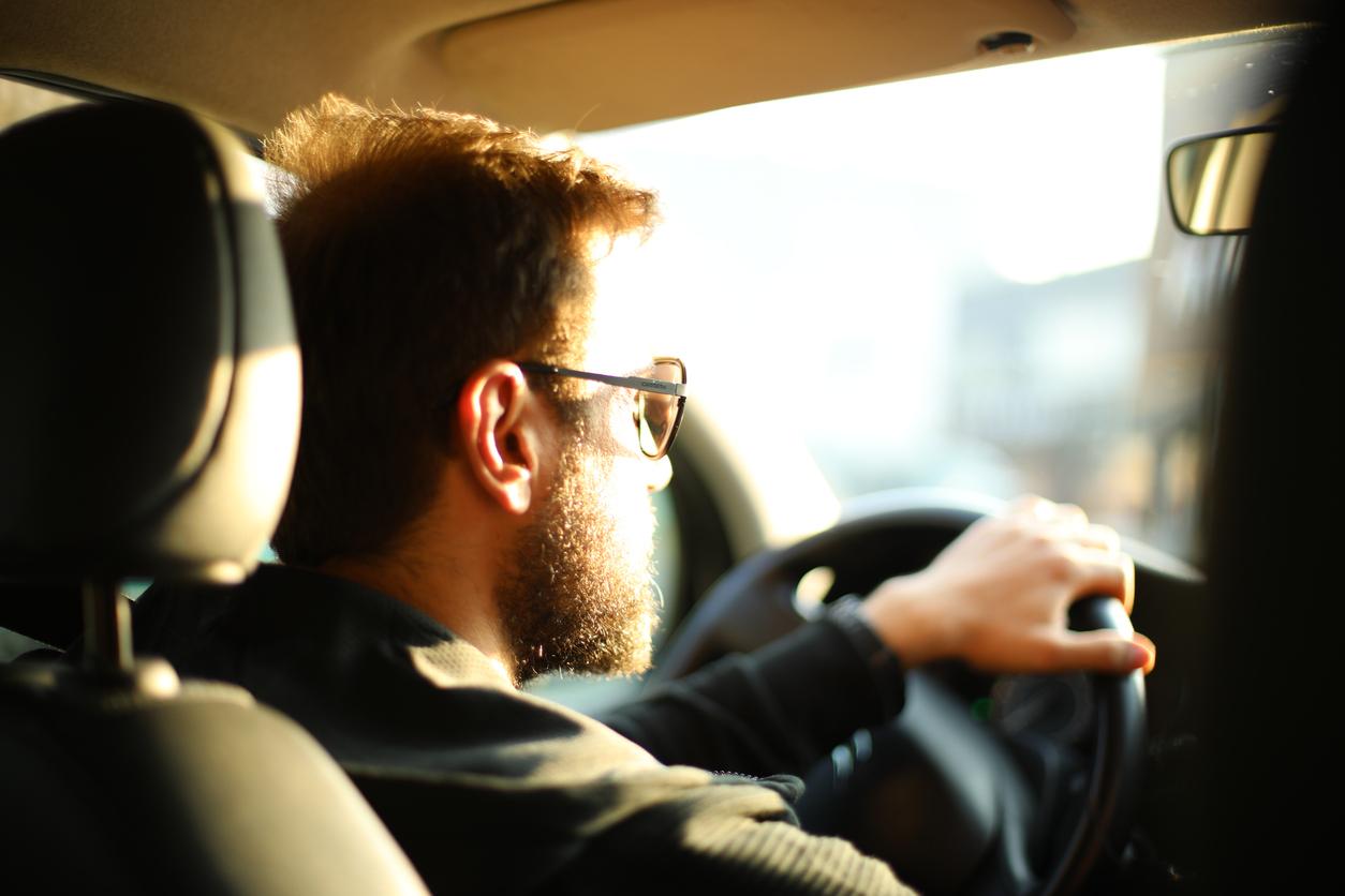 A male driver driving a car as seen from the back seat.