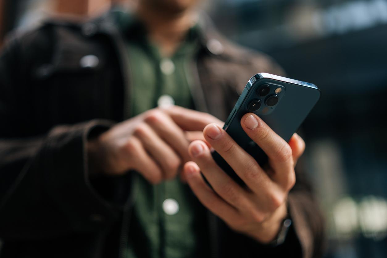 A man in a brown jacket and green shirt tapping a button on his smartphone.