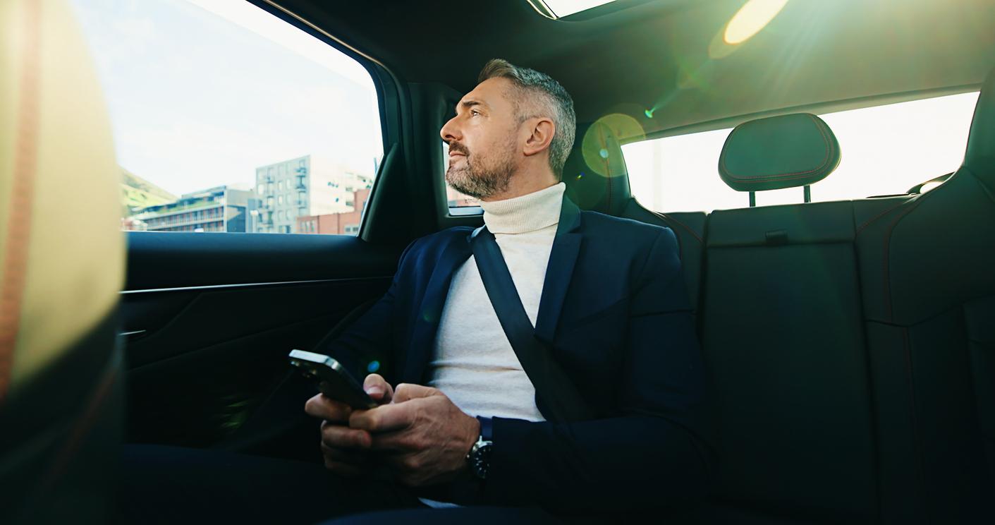A male passenger sitting in the back seat of a rideshare with his phone out