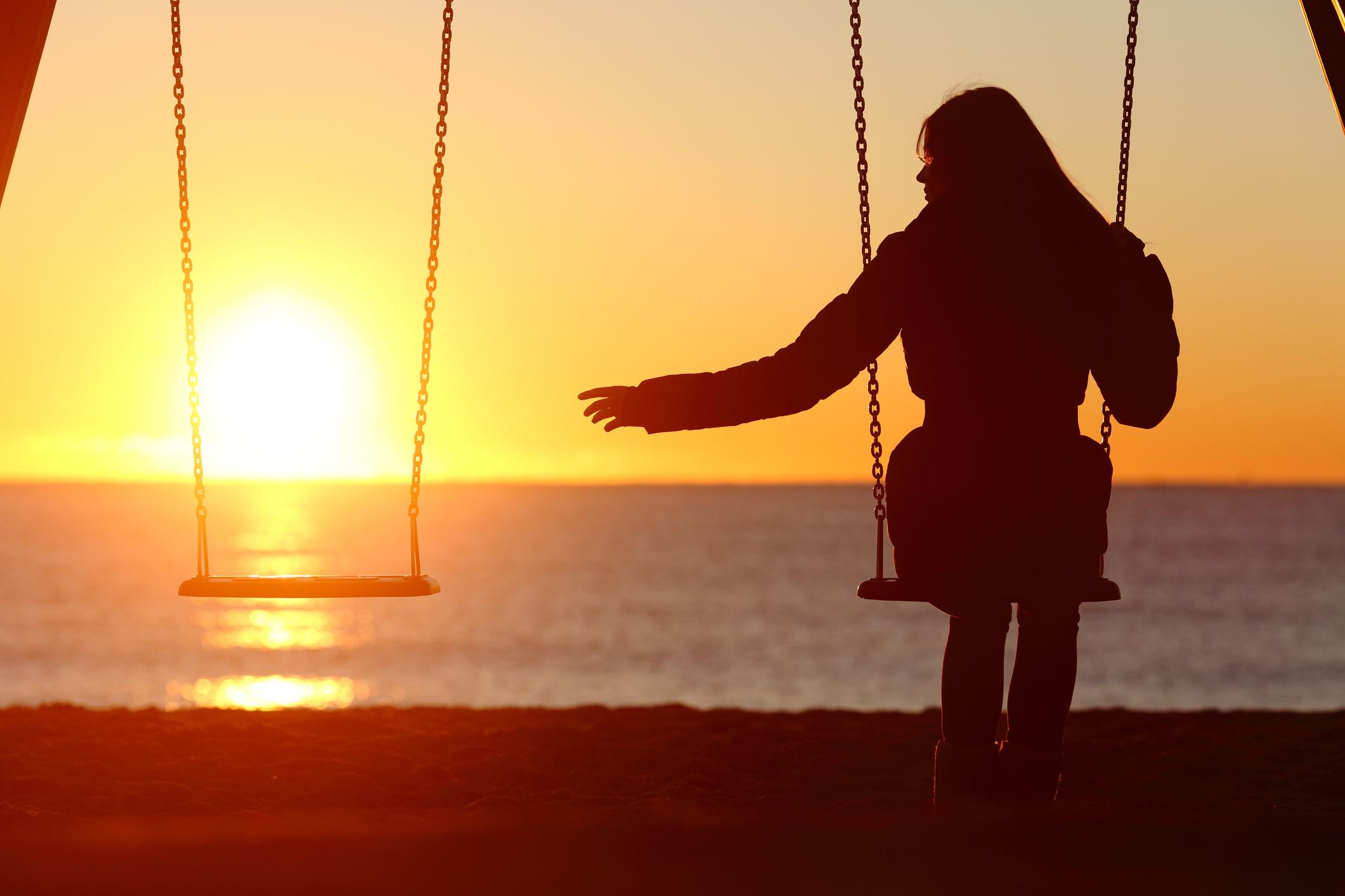 A widow sitting on a swingset at sunset reaching for the other empty seat, symbolizing wrongful death of a spouse
