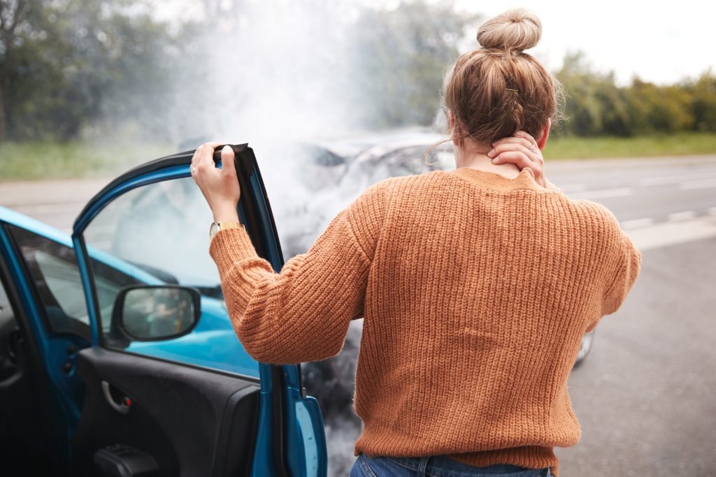 A woman standing by her car after a car accident holding the back of her neck