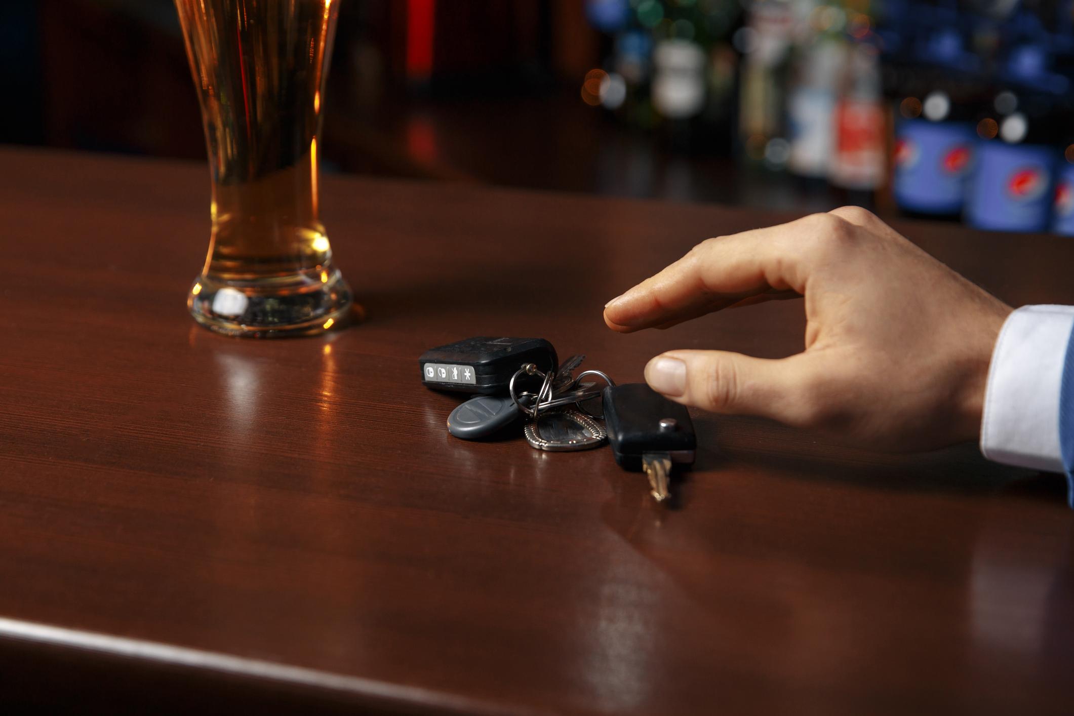 A person reaching for their car keys on a bartop with a beer in a glass