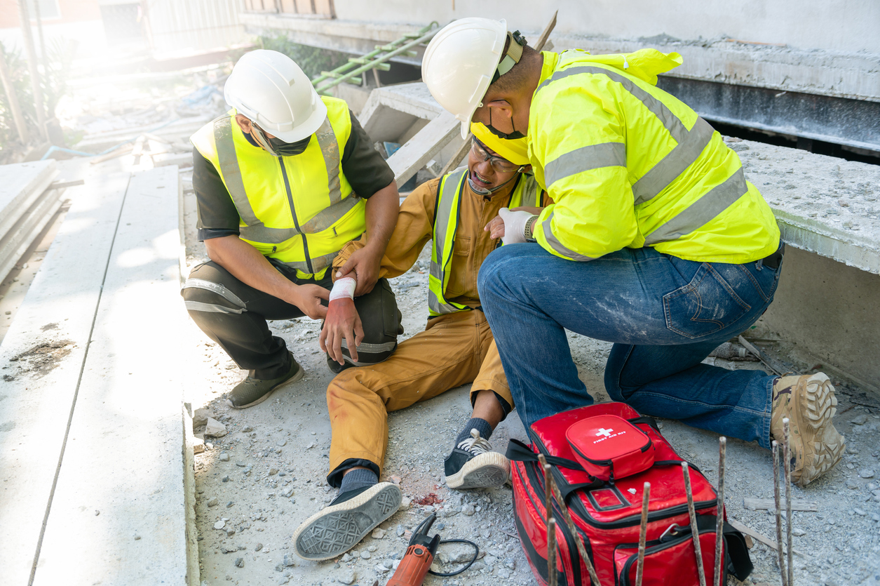 Two individuals giving first aid to an injured construction worker