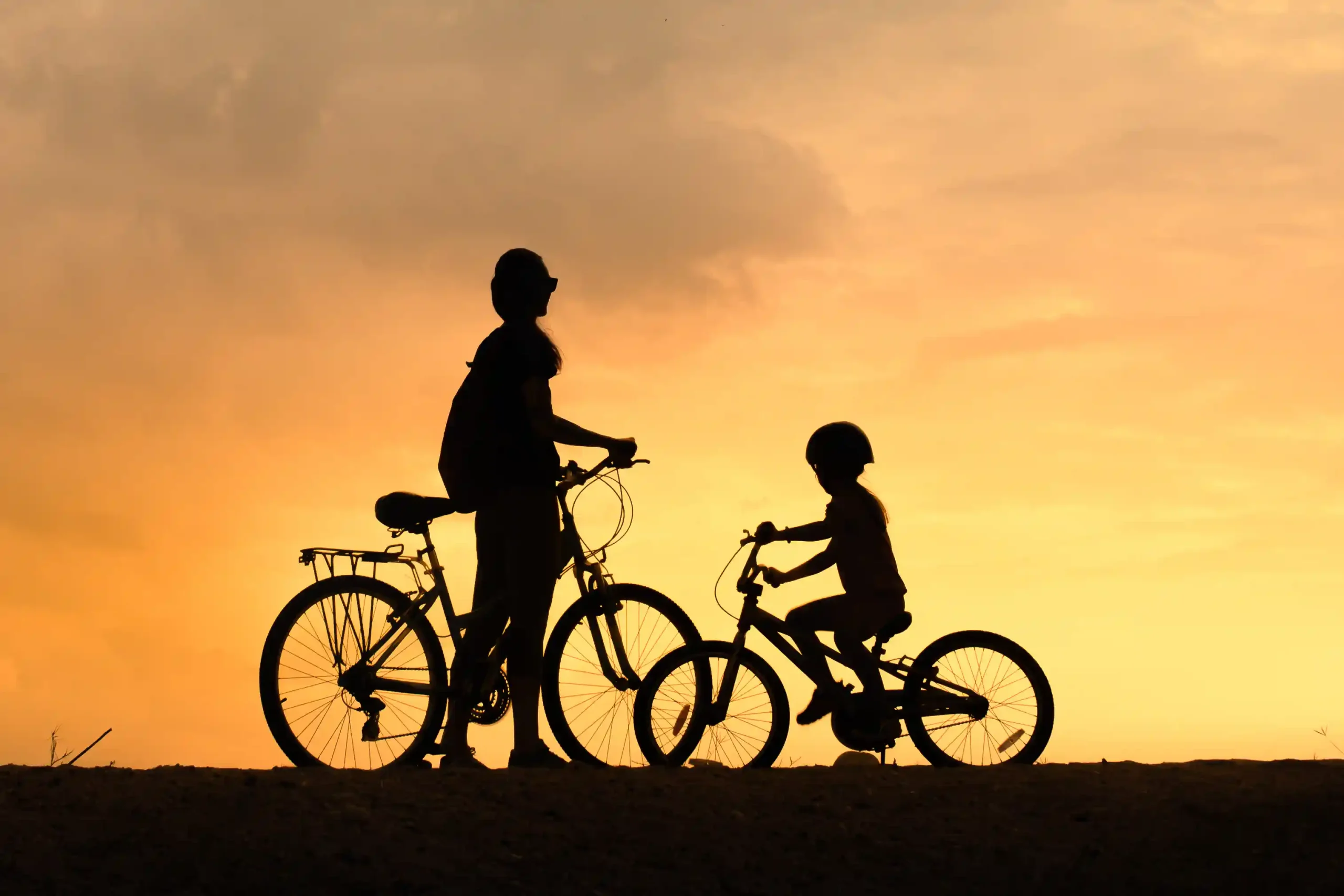 Silhouette of a mother and child on bikes at sunset