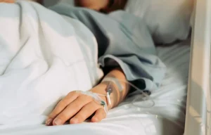 A person laying in a hospital bed with an IV in their arm