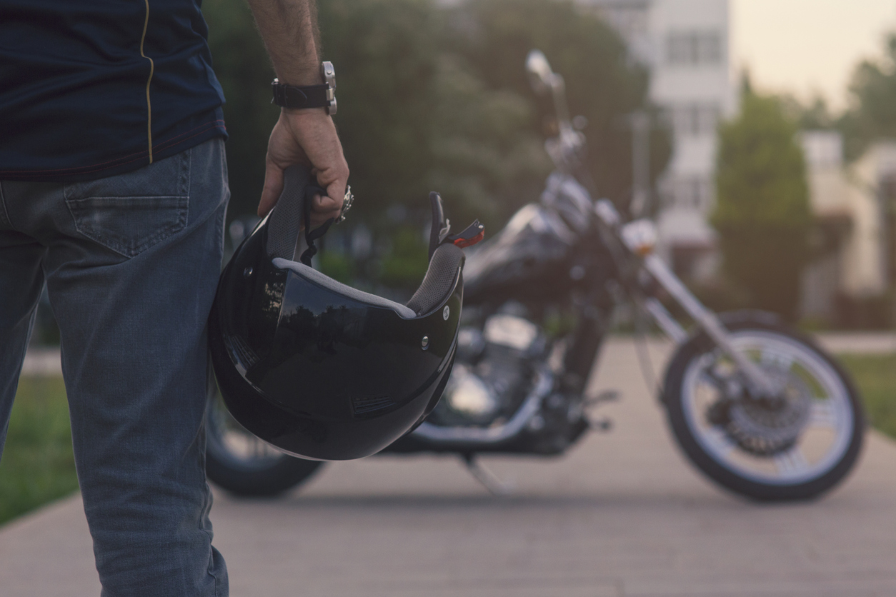 A motorcyclist standing in front of their motorcycle holding a helmet